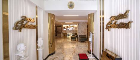 A hotel reception area with marble flooring, gold accents, and classical sculptures.