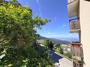 Zona residencial com vista para montanhas distantes, céu claro e uma varanda com grades de madeira.