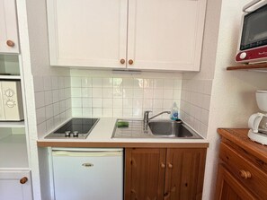 A compact kitchen with white cabinets, a built-in microwave, a small refrigerator, and a sink with a soap dispenser.