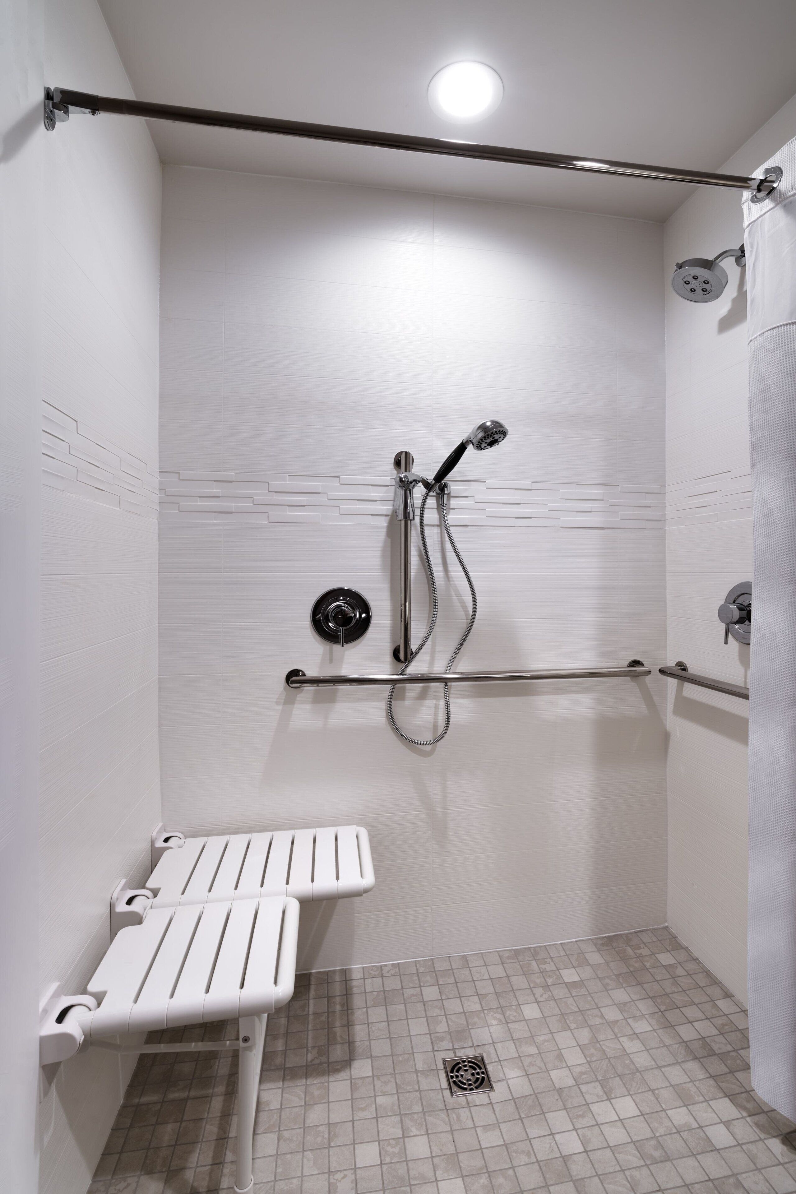 A small, white-walled shower with a handheld showerhead, a handheld shower attachment, and a grab bar.