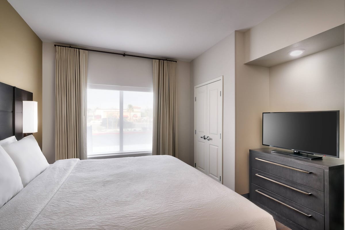 A hotel room with a large bed, a TV on a dresser, a wardrobe, and a window with curtains.
