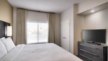 A hotel room with a large bed, a TV on a dresser, a wardrobe, and a window with curtains.