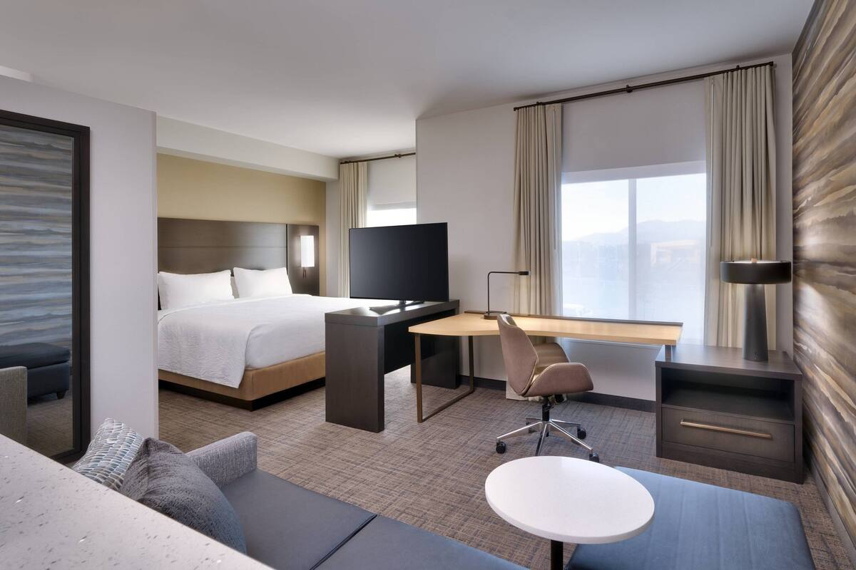A modern hotel room with a bed, desk, and seating area.