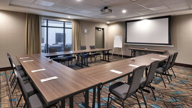 A conference room with a long table, chairs, a projector, a screen, and a view of the city through large windows. - Residence Inn by Marriott La Quinta (La Quinta)