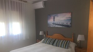 Ein Hotelzimmer mit einem Bett, zwei Nachttischen mit Lampen, einem Leuchtturm-Gemälde und einer Klimaanlage.