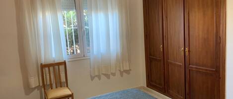 Un dormitorio con cama, un armario de madera, una silla y un ventanal con cortinas.