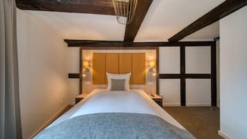 A hotel room with a large bed, wooden beams, a headboard with wall sconces, and a hanging light fixture.