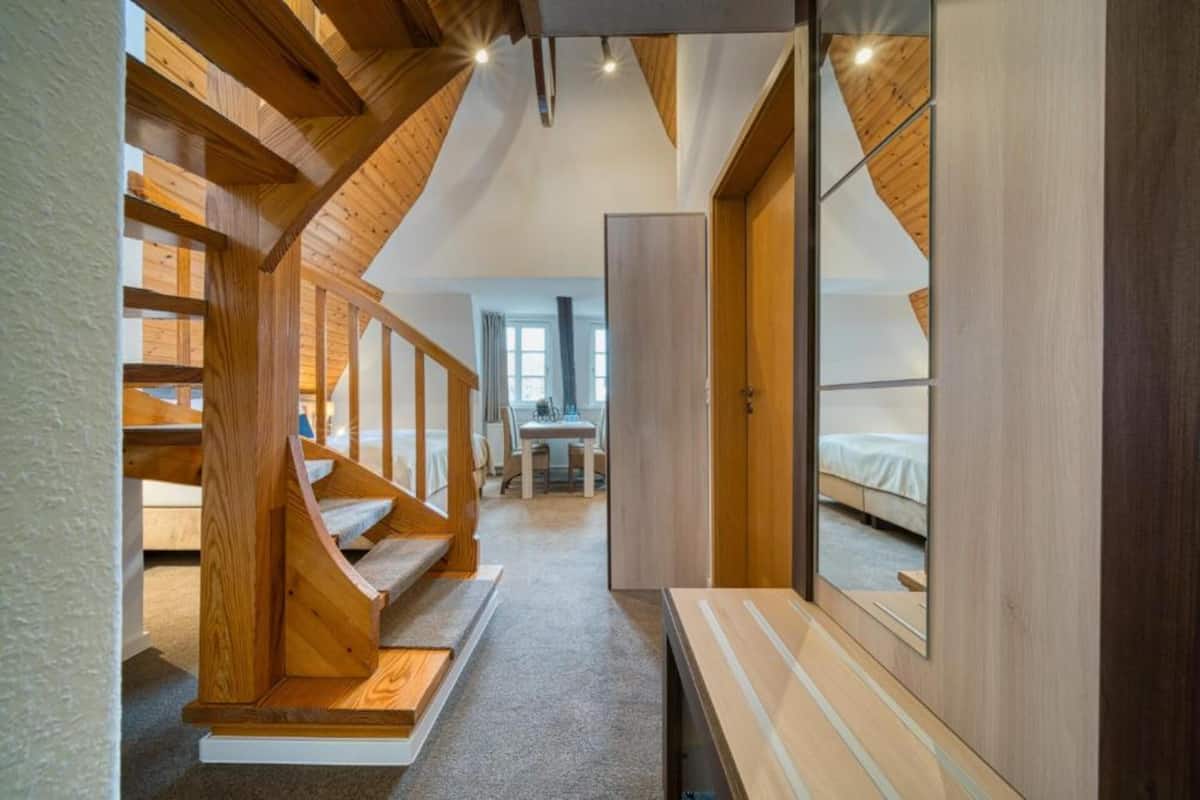 A narrow hallway with wooden staircases on either side, leading to a bedroom with a bed and a mirror.