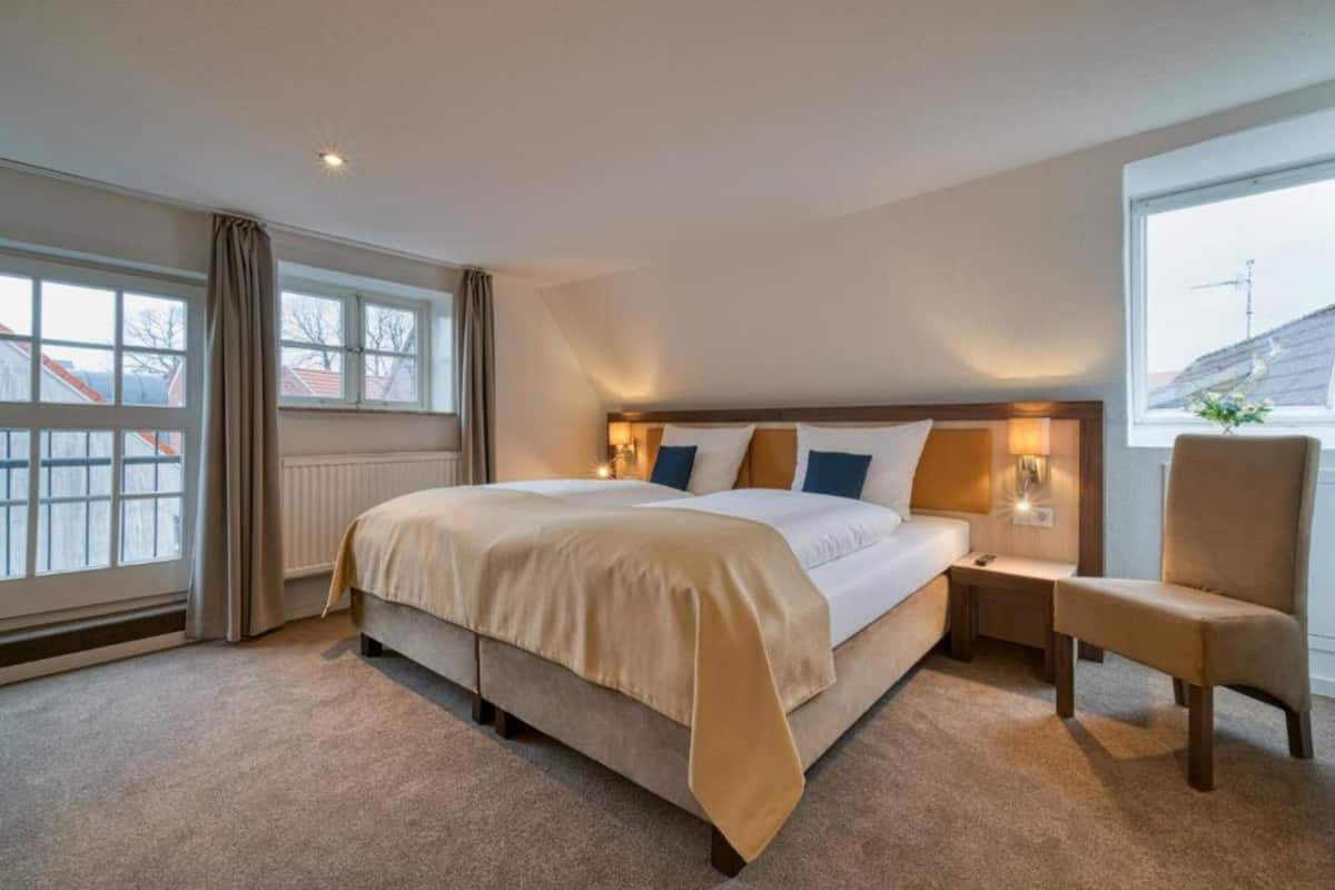 A hotel room with a large bed, a bedside table, a chair, and a window with curtains.