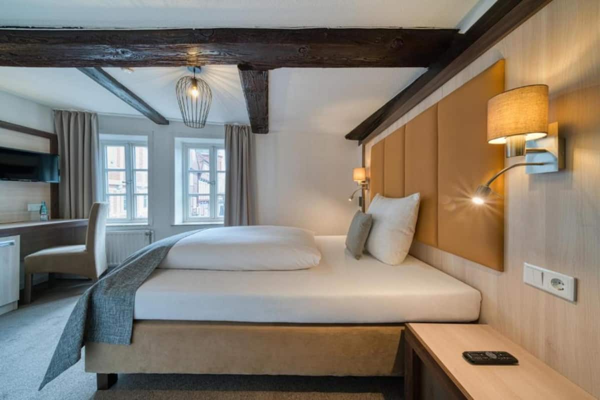 A hotel room with a large bed, a desk, a chair, a TV, and a window with curtains.