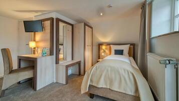 A hotel room with a bed, a desk, a chair, a television, and a window.