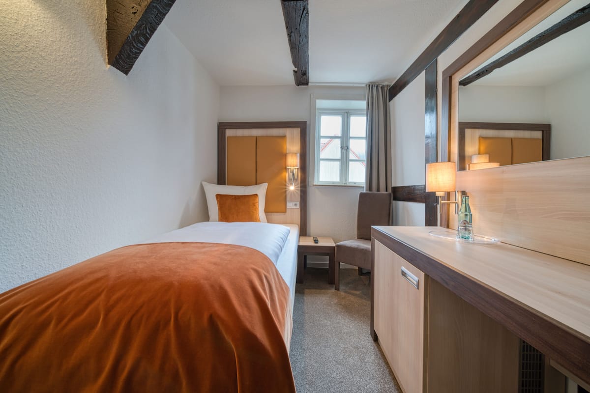 A hotel room with a bed, a desk, a chair, a mirror, and a window.