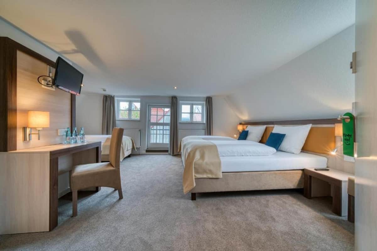A hotel room with a bed, a desk, a chair, a TV, and a window.