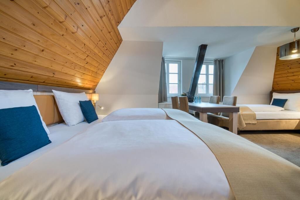 Habitación de hotel con dos camas, techo de madera, una mesa de comedor y una ventana.