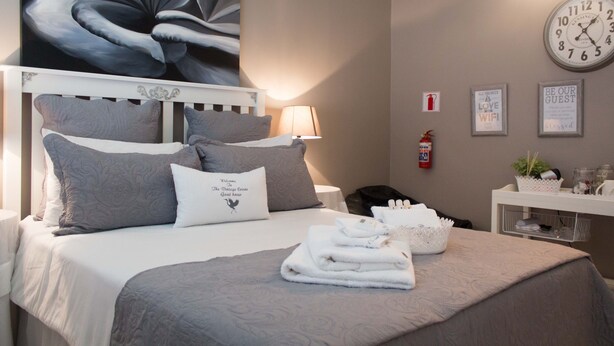 Een net opgemaakt bed met grijze beddengoed, een bedlampje, een klok en een bord met een welkomstboodschap.
