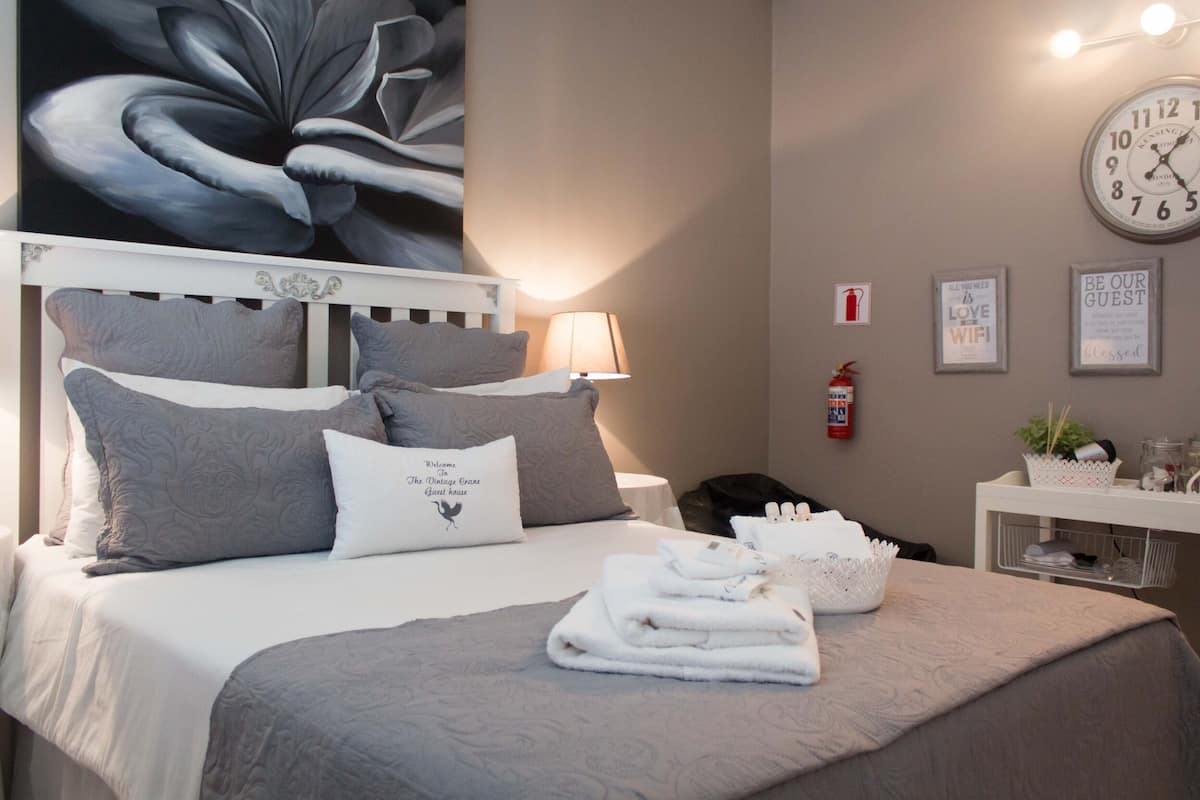 Una cama bien hecha con ropa de cama gris, una lámpara de noche, un reloj y un cartel de bienvenida enmarcado.