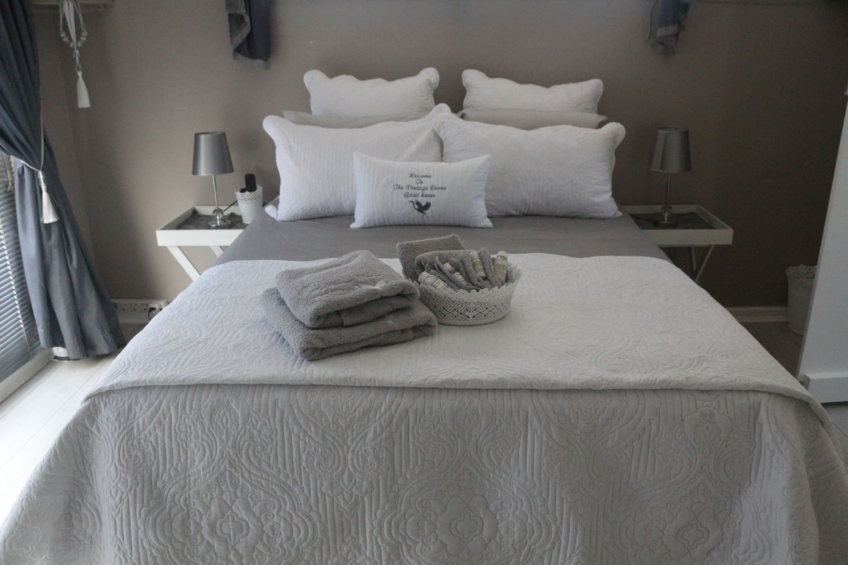 Una cama bien hecha con una colcha estampada, un juego de toallas dobladas y una almohada decorativa con texto.