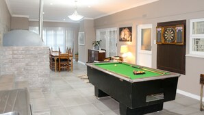 Een biljarttafel in een ruimte met een eethoek, een open haard en dartborden aan de muur.