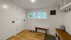 Una habitación con piso de madera, una puerta blanca, una ventana que da a zonas verdes, un banco y un letrero en la pared.