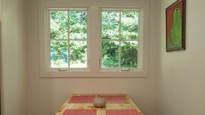 Una habitación con una mesa de madera, dos ventanas y un jarrón.