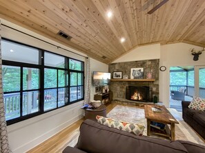 A cozy living room with a fireplace, large windows, and a stone wall. - Secluded, Stylish & Completely Reimagined | Azalea at Highlands Falls (Highlands)