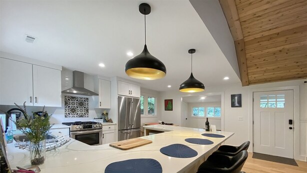 Una cocina moderna con una isla grande, electrodomésticos de acero inoxidable e iluminación colgante negra.