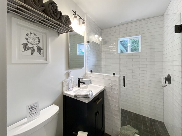 A modern bathroom with a white tiled shower, a black vanity, a white toilet, and a dreamcatcher decoration. - Secluded, Stylish & Completely Reimagined | Azalea at Highlands Falls (Highlands)