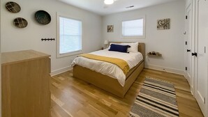 Un dormitorio con cama, dos ventanas, ventilador de techo y cómoda de madera.