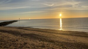Une plage avec une digue rocheuse et des eaux calmes qui reflètent le coucher de soleil.