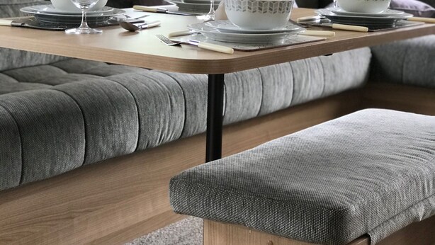 Un espace repas avec une table en bois dressée pour quatre personnes, entourée de sièges rembourrés de couleur grise.