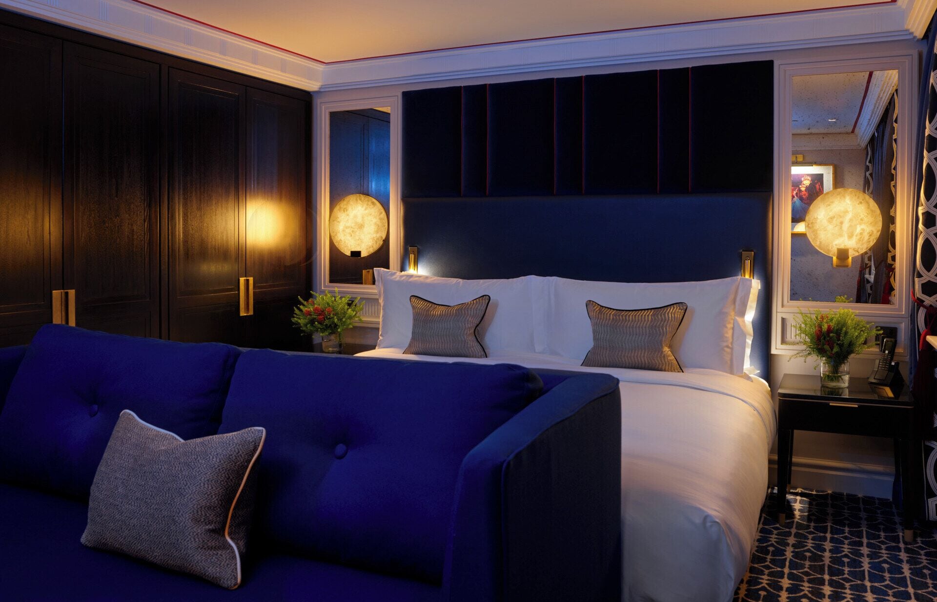 A hotel room with a large bed, dark wood paneling, a blue sofa, and two wall-mounted lamps.