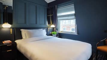 A hotel room with a large bed, a nightstand with a lamp, a window with curtains, and a view of a building outside.