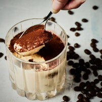 Ein klares Dessertglas mit einem Löffel dunkler Soße, umgeben von verstreuten Kaffeebohnen.