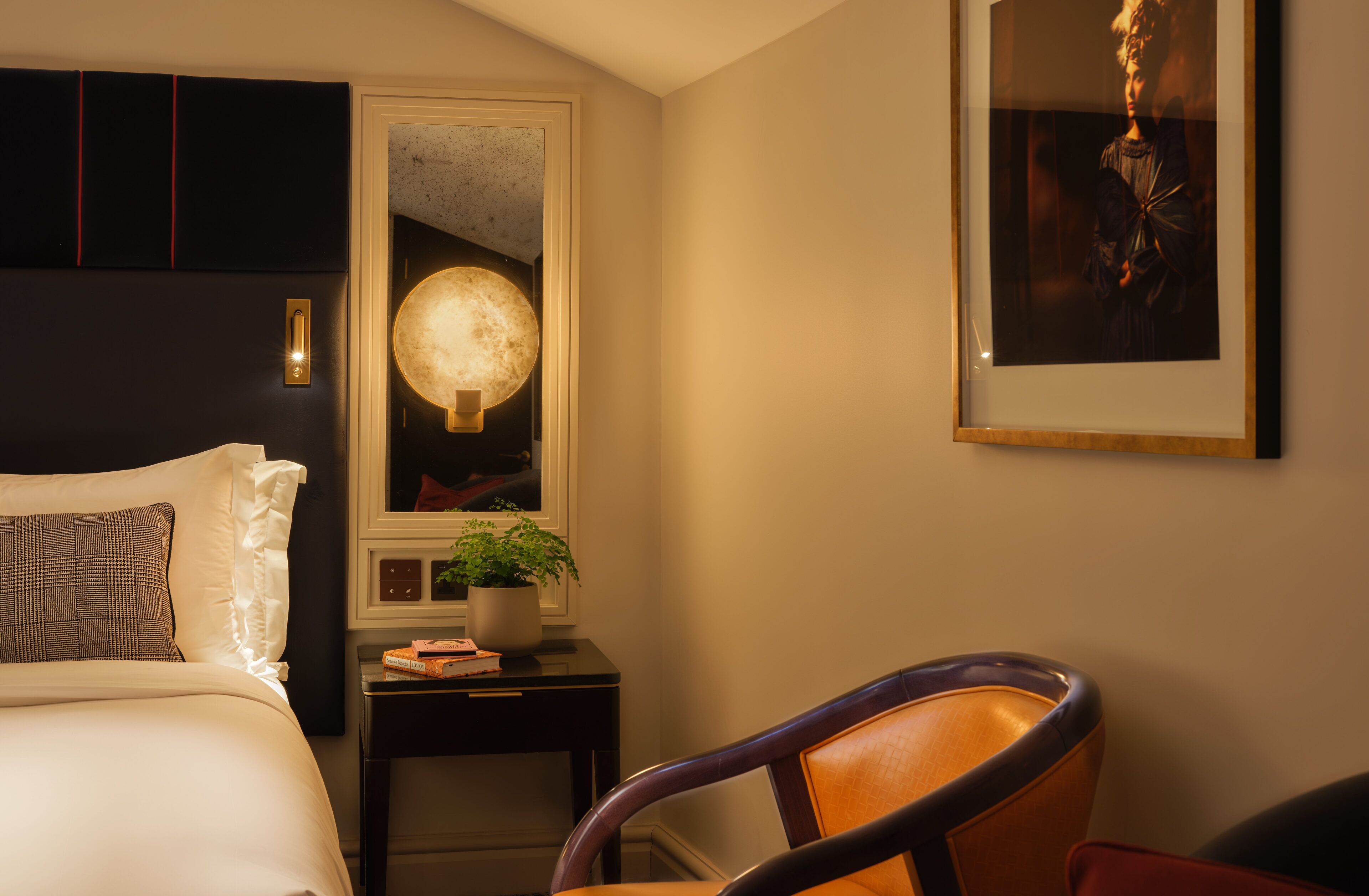 A hotel room with a bed, a nightstand with a lamp, a framed picture, and a chair.