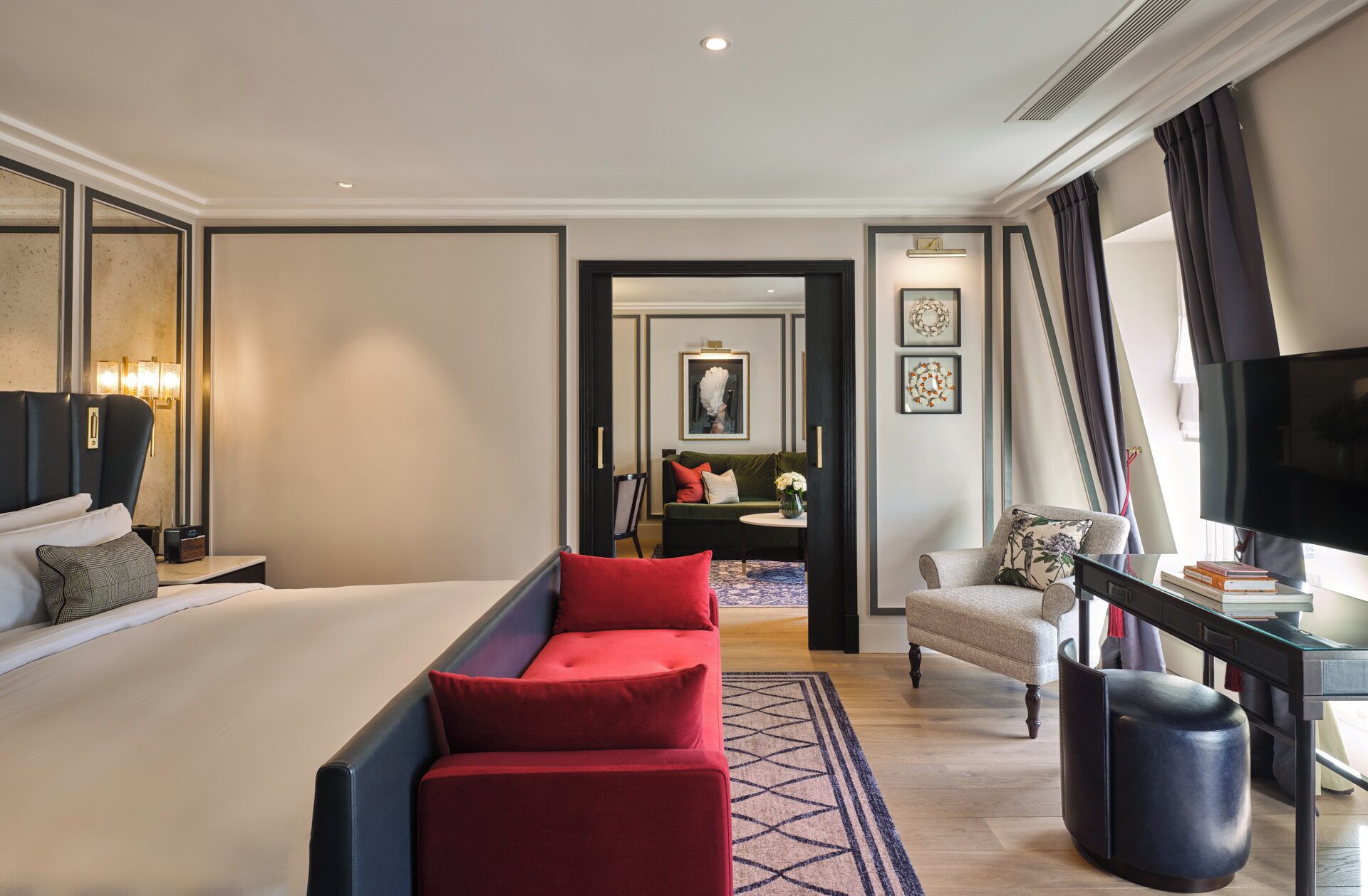 A hotel room with a large bed, a red sofa, a desk with a TV, and a small table with books.