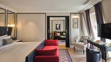 A hotel room with a large bed, a red sofa, a desk with a TV, and a small table with books.