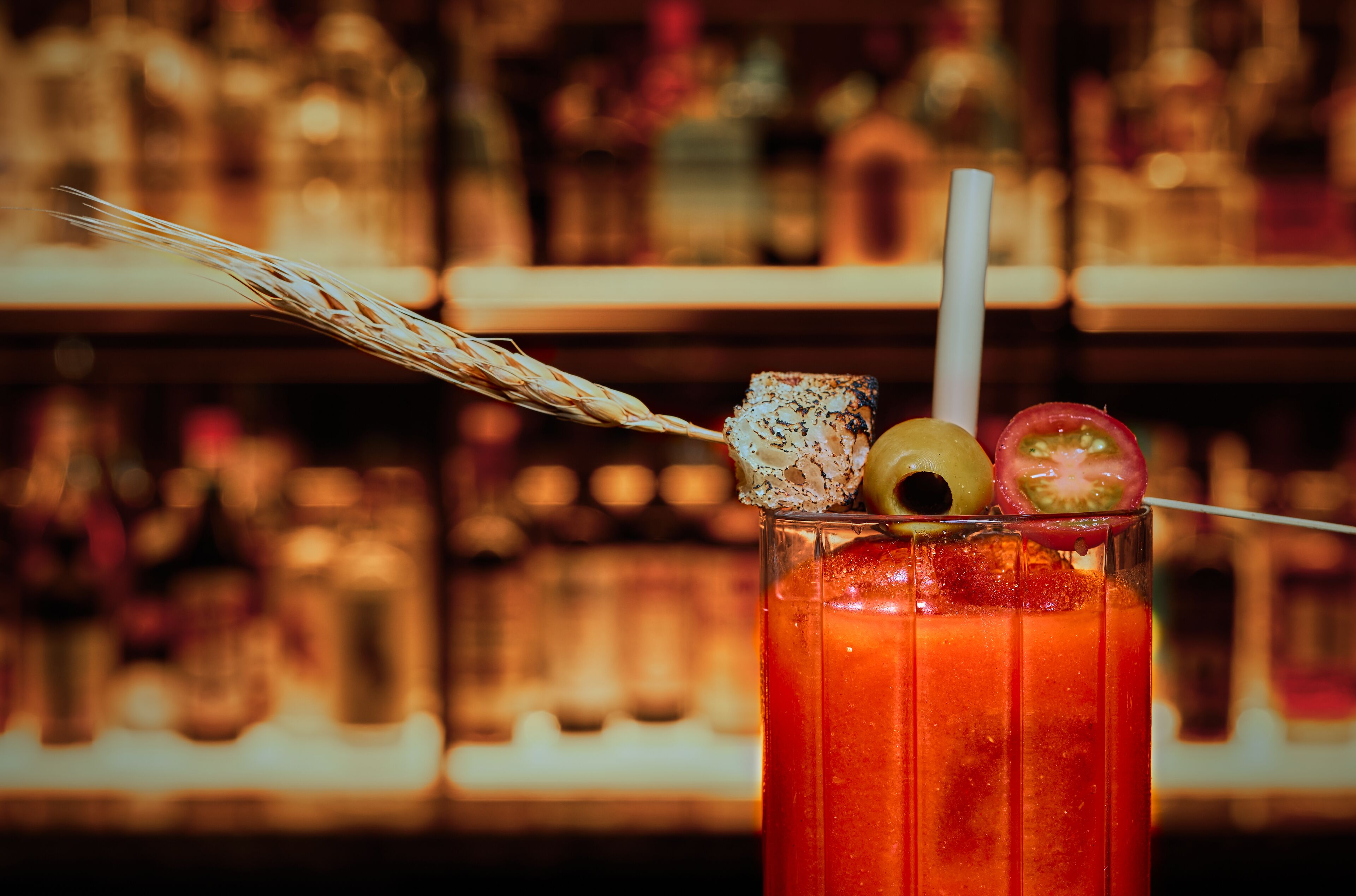 A tall glass with a straw, garnished with a slice of lime, a cherry, and a small olive.