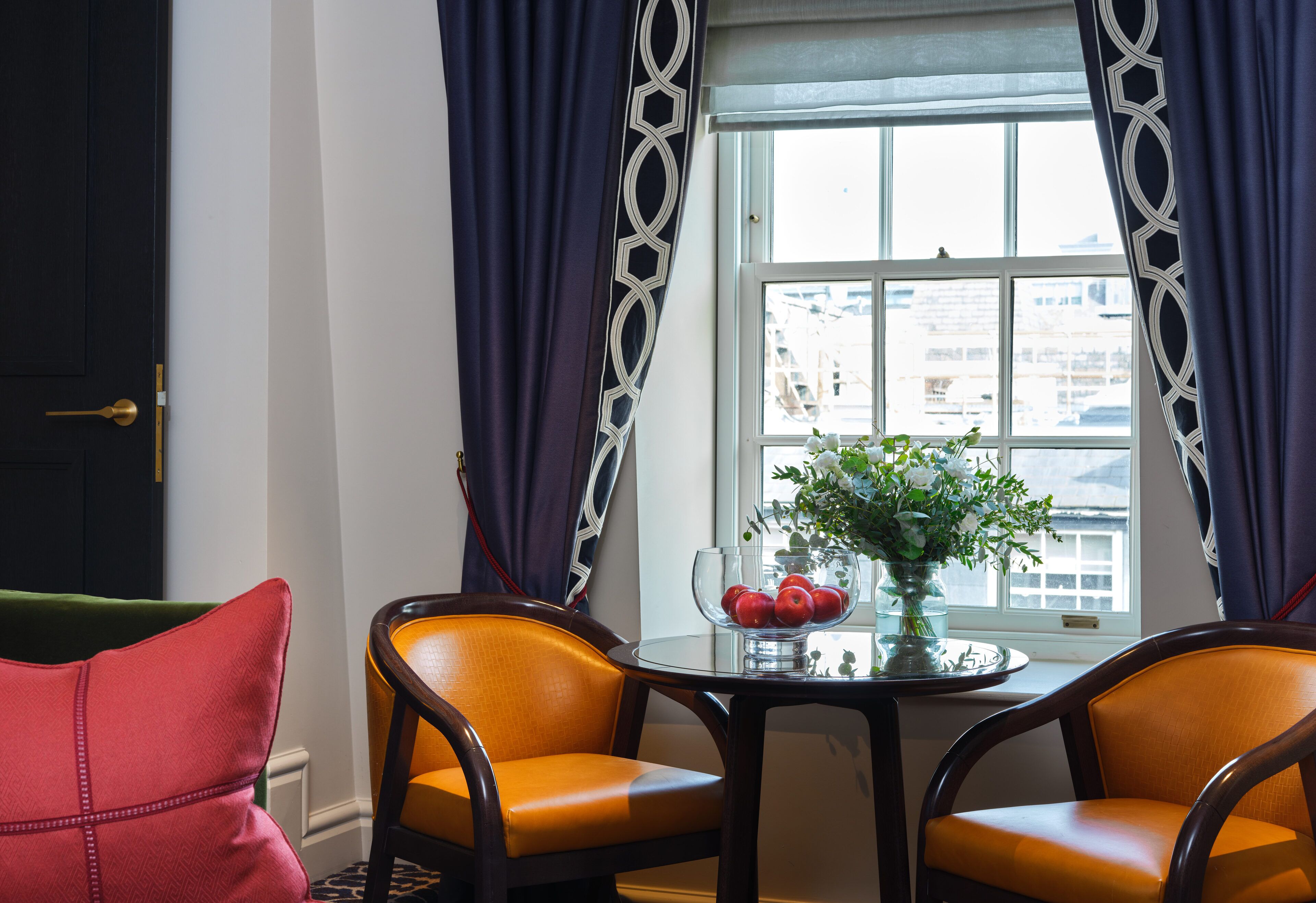 A room with a table set for two, a vase with flowers, and a window with curtains.