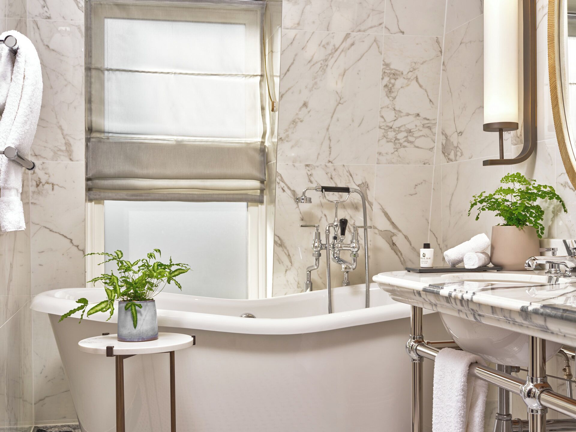 Une salle de bain moderne avec une baignoire sur pieds, un meuble-lavabo doté d’un plan de travail en marbre et une plante en pot posée sur une petite table.