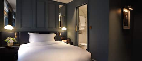 Ein Hotelzimmer mit einem großen Bett, einem Nachttisch mit Lampe, einem Spiegel und einem gerahmten Bild an der Wand.