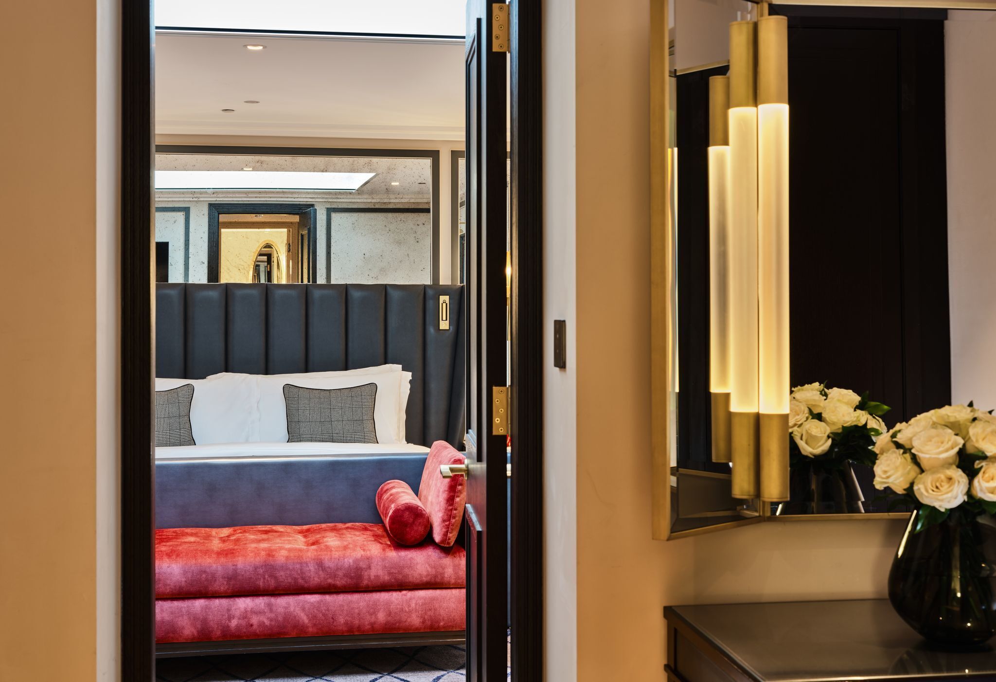 A hotel room with a bed, a red sofa, a mirror, and a vase with flowers.