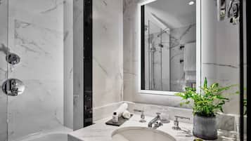 Un baño moderno con lavamanos de mármol, un espejo grande, ducha y una planta en maceta.