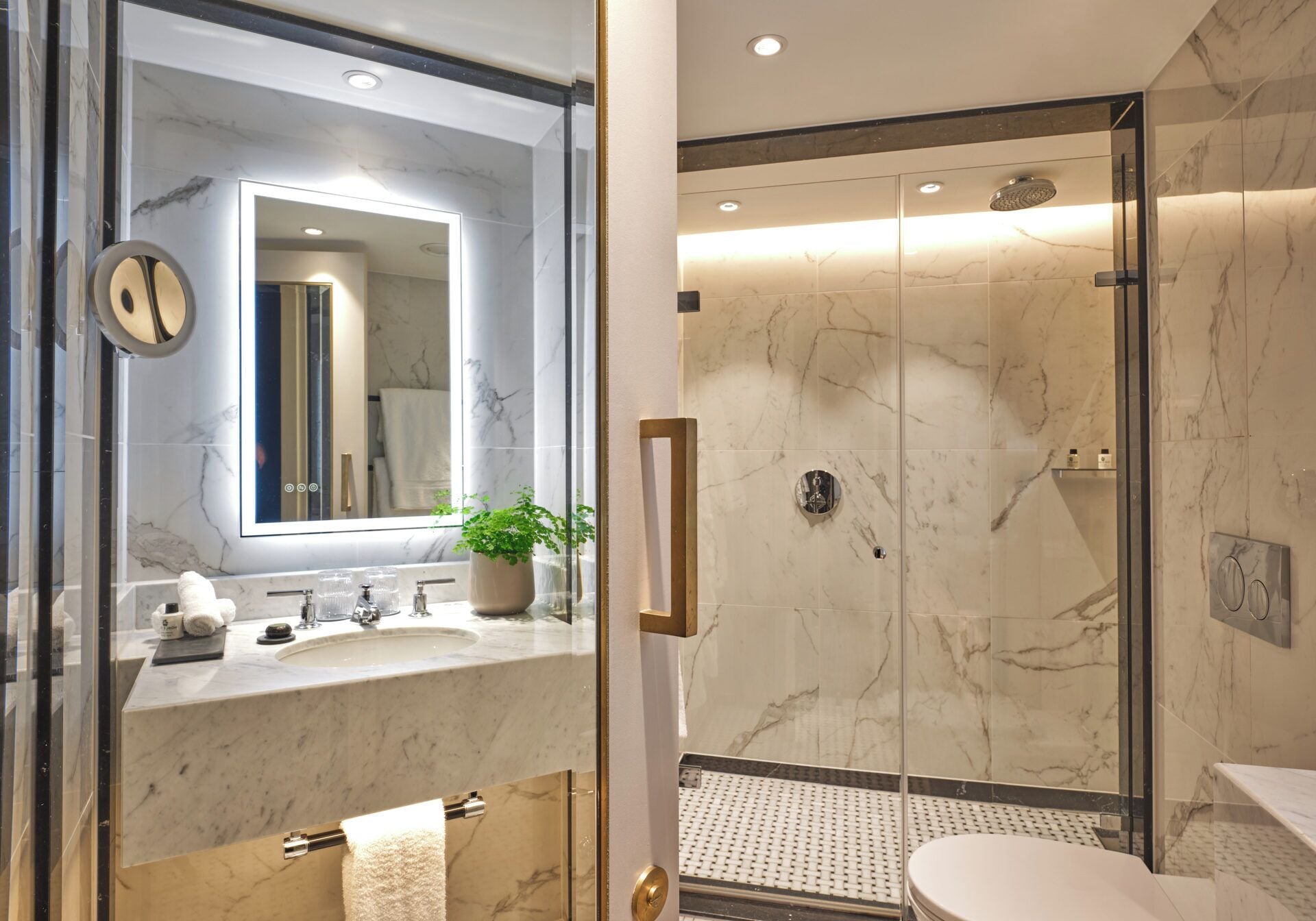 A modern bathroom with a glass shower enclosure, marble countertops, and a large mirror.