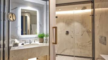 A modern bathroom with a glass shower enclosure, marble countertops, and a large mirror.