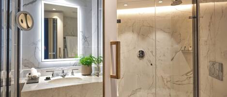 A modern bathroom with a glass shower enclosure, marble countertops, and a large mirror.