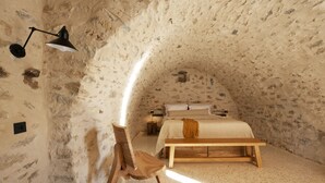 Ein Schlafzimmer mit schrägen Wänden, einem Bett, einem Holzstuhl, einer Bank und einer Schreibtischlampe.
