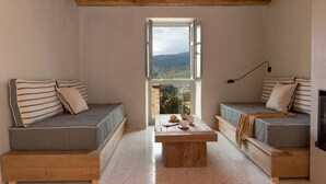 Ein gemütlicher Raum mit zwei Holzbanken, einem zentralen Tisch und einem Fenster mit Blick auf eine Berglandschaft.