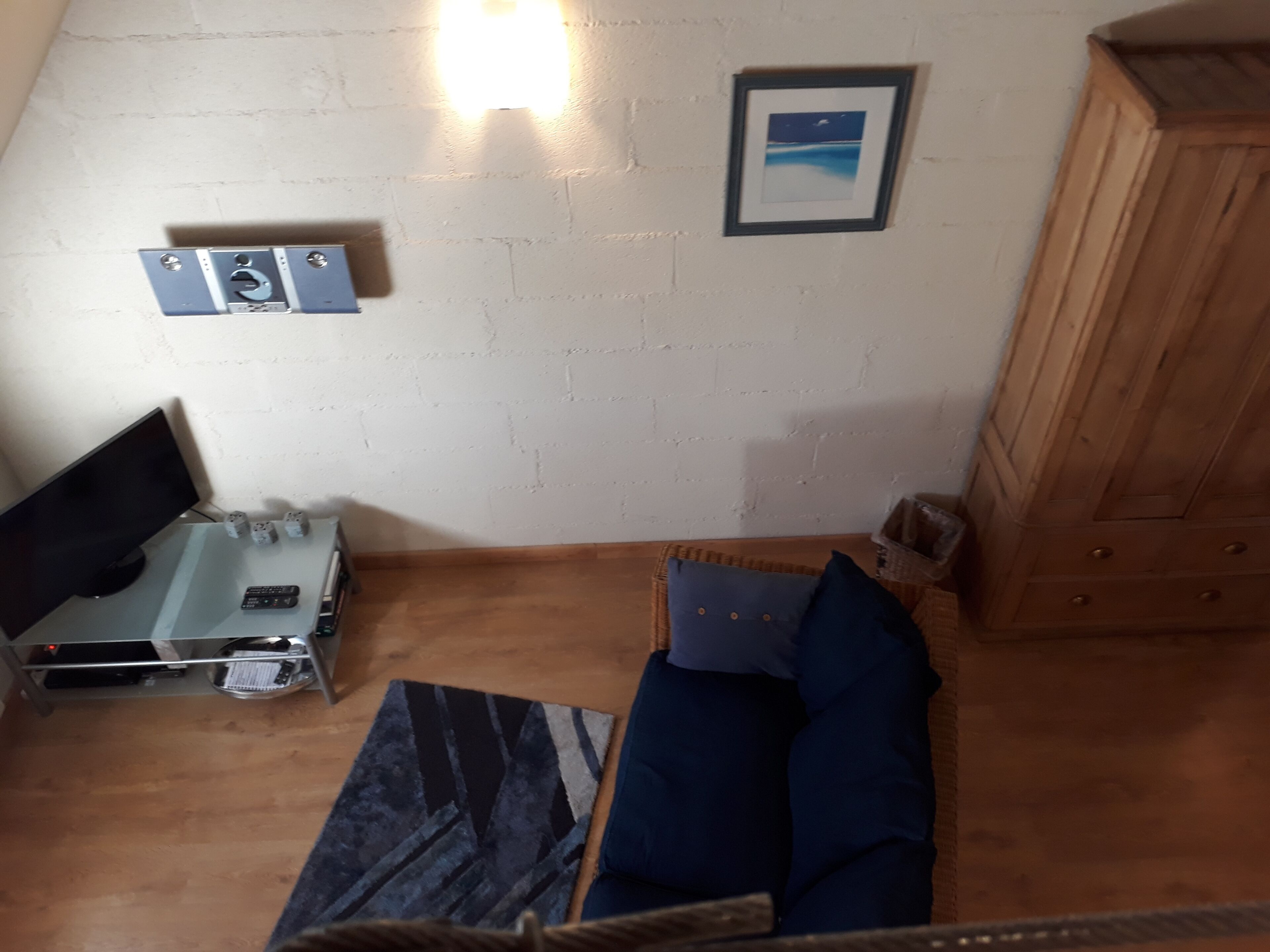 Et værelse med seng, fjernsyn, skrivebord med computer og tastatur, stikkontakt og et billede i ramme.