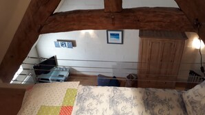 A room with a sloped ceiling, wooden beams, a bed with patterned bedding, a small table, and a wall-mounted picture.