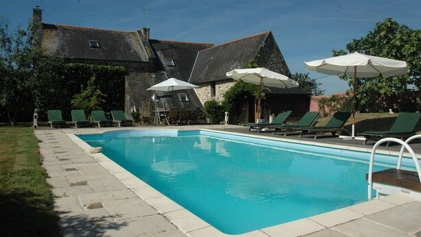 A swimming pool with lounge chairs and umbrellas, surrounded by stone buildings and greenery.